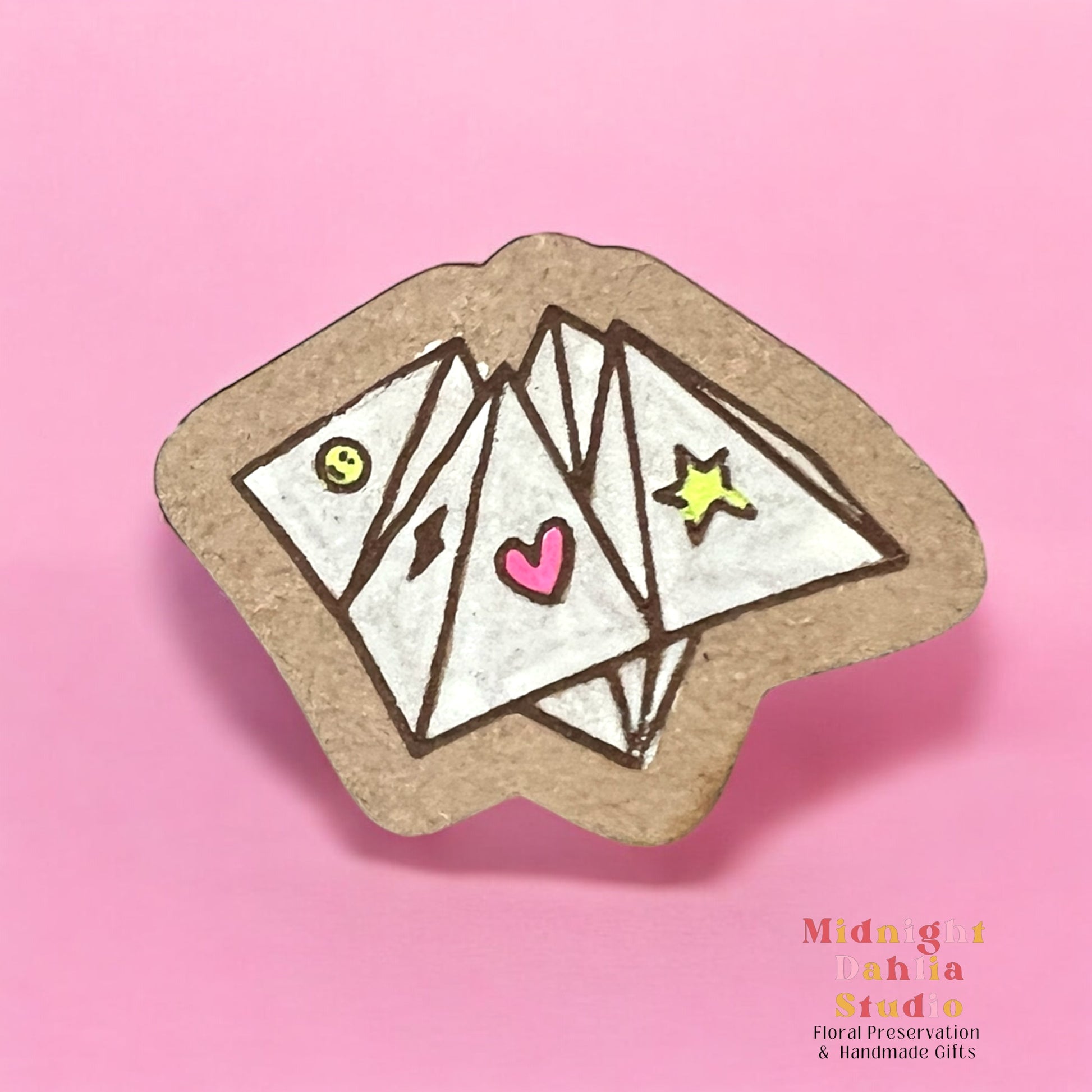 A wooden pin in the shape of a cootie catcher kid’s game in white with small bright symbols of a smile, lightning bolt, heart, and star