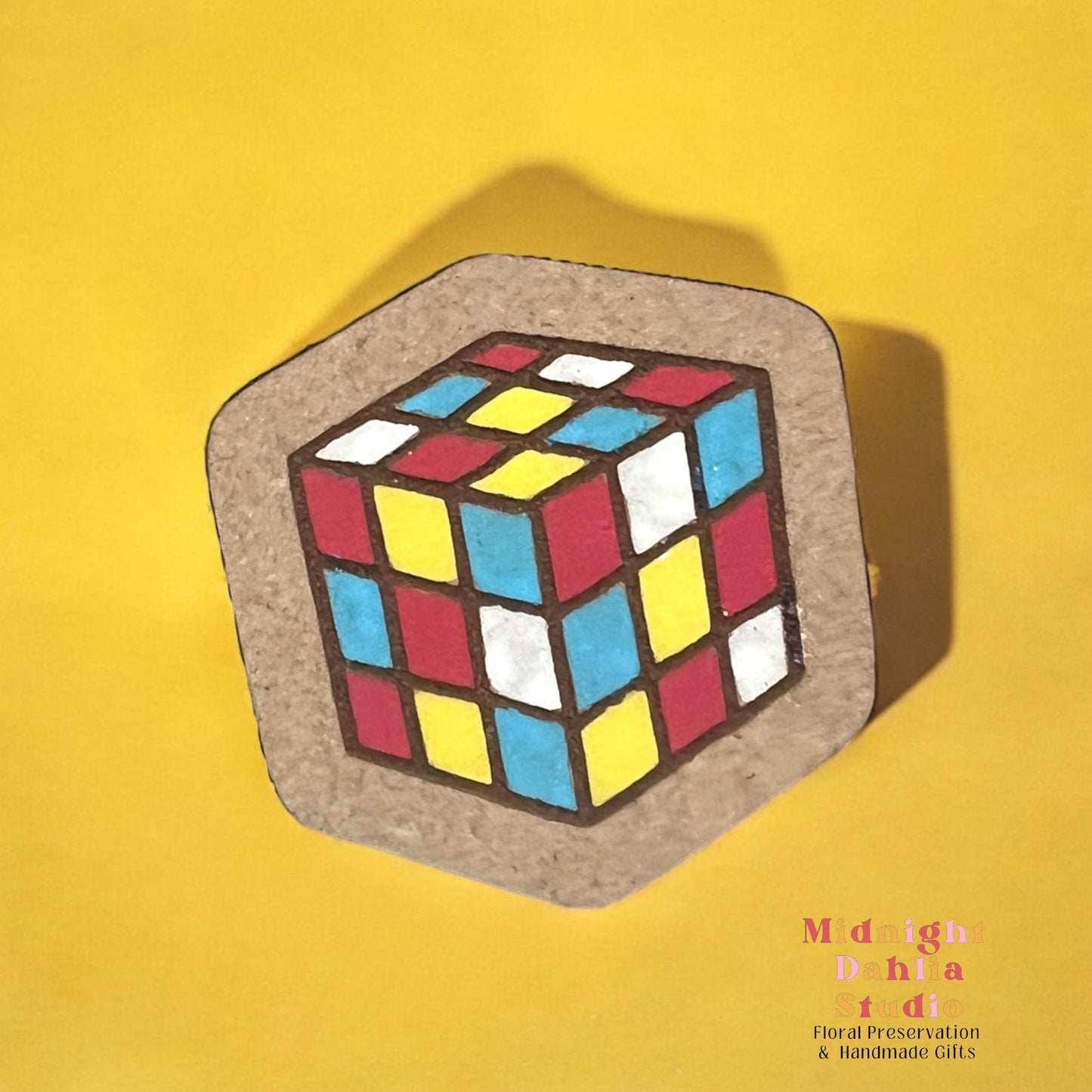 A wooden square pin with a painted Rubik’s cube with blocks of red yellow blue and white