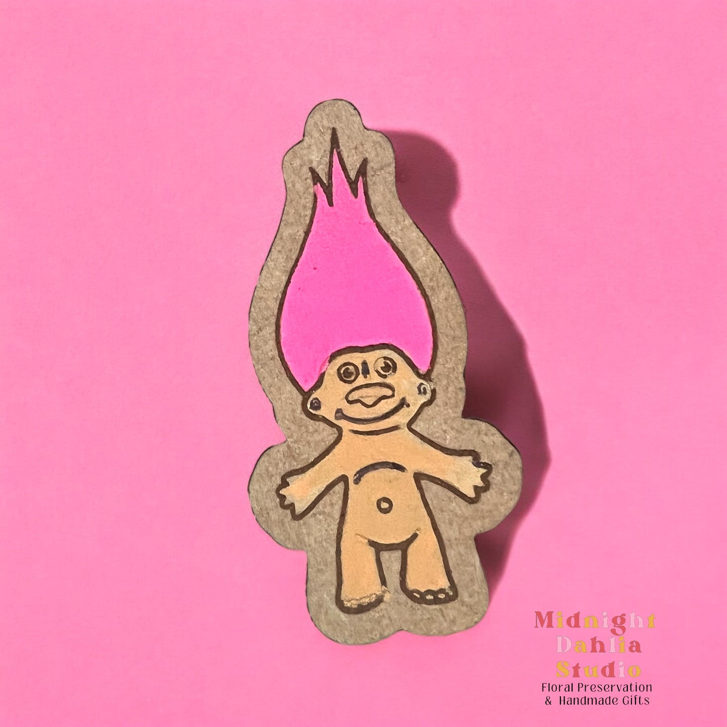 A wooden pin with a hand painted troll doll with peach skin and bright pink hair