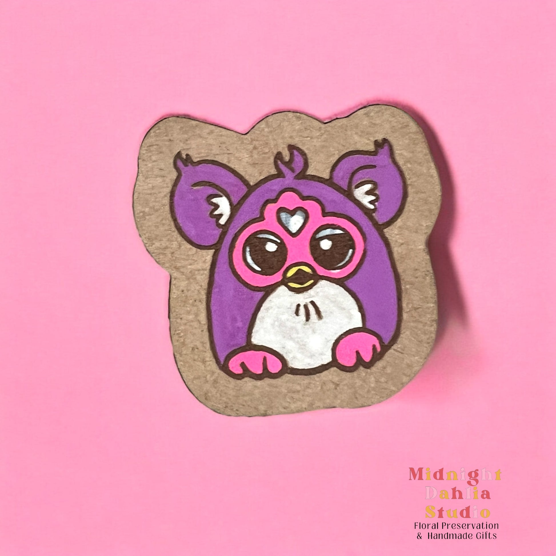 A wooden pin with a handpainted Furby toy animal that is purple and white with pink feet and face