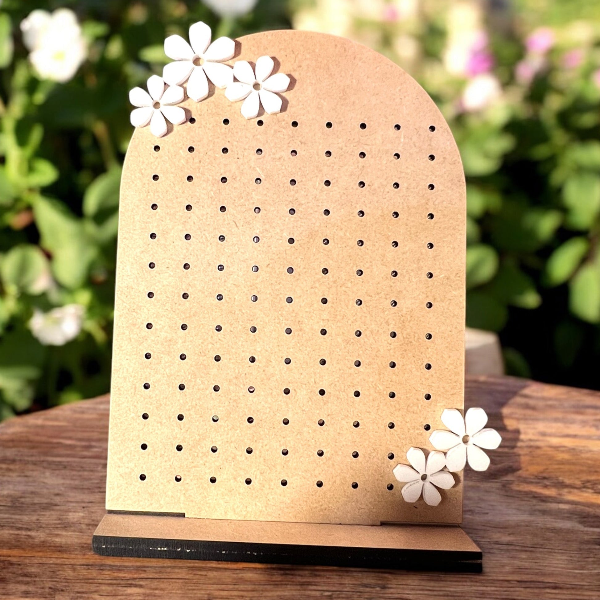 a wooden stand with holes carved in it for jewelry organization with white acrylic flowers