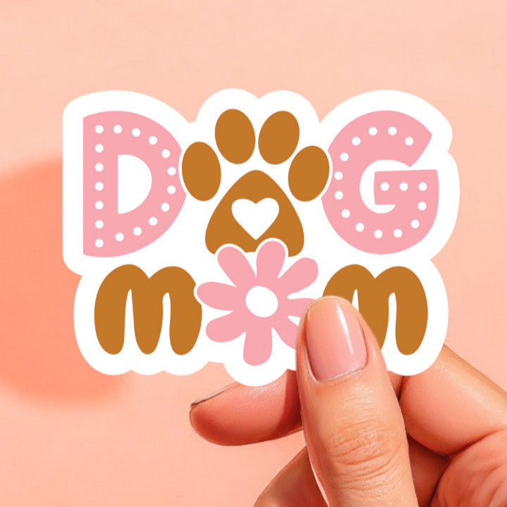 a white background sticker that reads dog mom with a paw print as the o in dog and a daisy as the o in mom.  the sticker is printed in brown and pink.