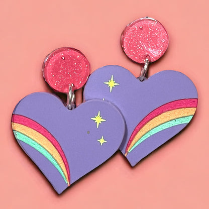 Acrylic earrings in the shape of a heart made of lavender acrylic with a rainbow of hot pink, orange, and mint green with yellow stars, on a hot pink glitter hardware.  perfect gift for pride and every day for women.