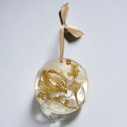 A crystal clear circle resin christmas ornament with yellow tulips and stock , with an off-white ribbon.  A beautiful add-on for a bridal bouquet preservation.