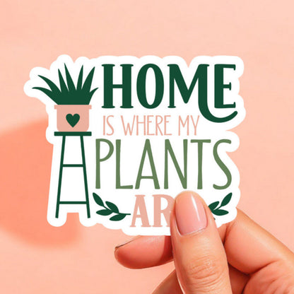 a white background sticker that reads home is where my plants are in green and peach with a plant on a stand on the left side