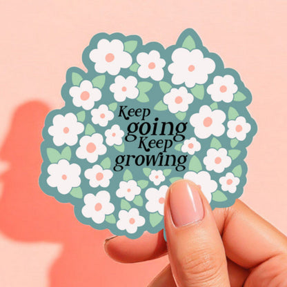 a sticker with a light blue background that reads keep going keep growing surrounded by white daisies