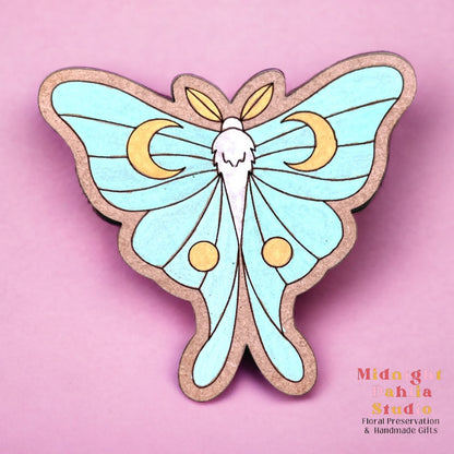 a wooden luna moth magnet hand painted in teal, yellow, and white