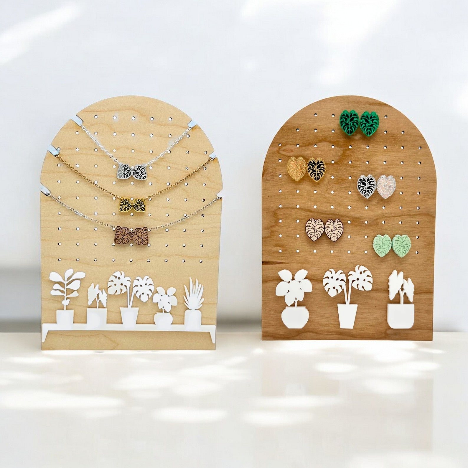 two arch shaped wooden jewelry organizers with holes for necklace and earring organization with white acrylic plants along the bottom.