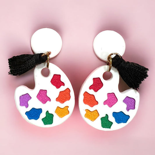 a paint palette shaped earring with multi colored blobs to resemble paint and a black tassel to look like a paint brush.  a perfect gift for an artist or art teacher.