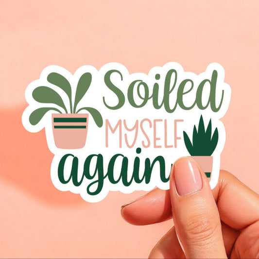 a white sticker that reads soiled myself again with two potted plants in green and peach light brown