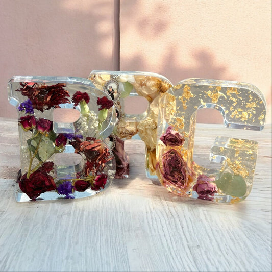 A collection of resin letters with dried preserved flowers , including a rose , a carnation , mini spray roses , and other white red and pink flowers.  A beautiful way to preserve your bridal bouquet.