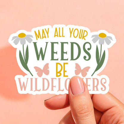 a white sticker that reads may all your weeds be wildflowers in pink green and yellow with a white daisy and pink butterfly on either side