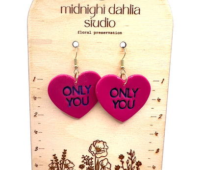 heart shaped earrings with only you stamped in purple.  they are on gold fish hook style earrings.  they are hanging on a wooden arch style background that reads midnight dahlia studio and has florals on the bottom and measurements on either side.  the earrings hang down to just over 2".