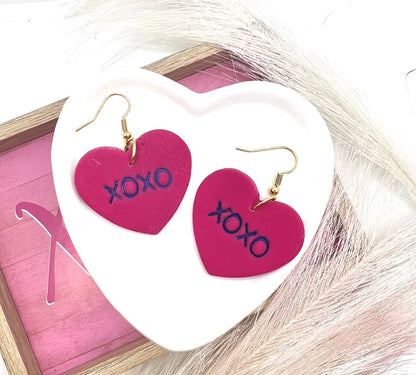 heart shaped earrings stamped with XOXO in purple on a gold fish hook style earring.