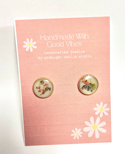 these are round gold stud earrings filled with tiny bits of flowers on various colors on a white background.