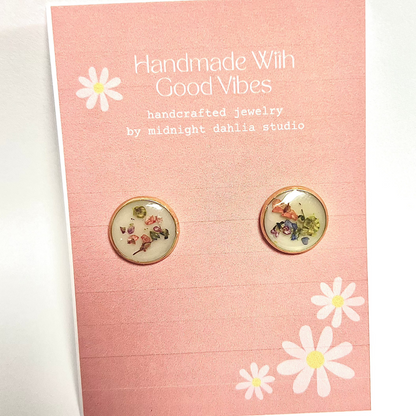 these are round gold stud earrings filled with tiny bits of flowers on various colors on a white background.